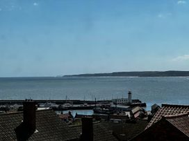 A harbor with boats and a lighthouse near the sea with rooftops in the foreground at Launcher's Cottage in Scarborough