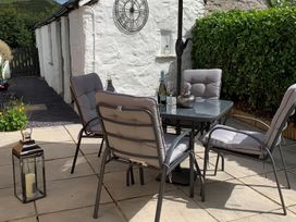 An outdoor seating area with a glass table four chairs lantern and a bottle with two glasses at Cartref in Llangernyw