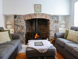 A living room with a stone fireplace wooden floor gray sofas and an ottoman at Cartref in Llangernyw