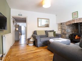 A living room with a gray sofa, a stone fireplace with fire, a mirror above the sofa, wooden floor, and a TV on the wall at Cartref in Llangernyw