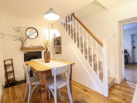 A dining area with a wooden table and four chairs next to a staircase and a small shelf with books at Cartref in Llangernyw