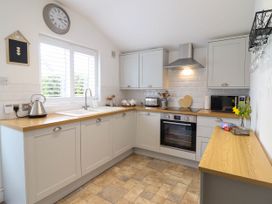 A kitchen with light gray cabinets wooden countertops a clock above the window and stainless steel appliances at Cartref in Llangernyw