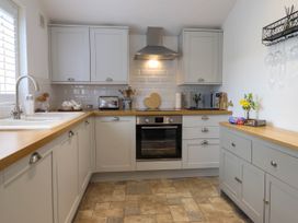 A kitchen with a built in oven stovetop wooden countertops grey cabinets a microwave a toaster a sink and a vase with flowers at Cartref in Llangernyw