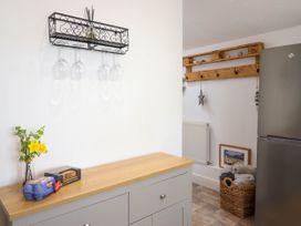 A kitchen corner with a wooden countertop, a wine glass rack, a refrigerator, a wall-mounted coat rack, and a woven basket with blankets at Cartref in Llangernyw