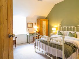 A bedroom with a white metal bed frame bedside tables a wooden wardrobe and a desk at Cartref in Llangernyw