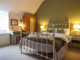 A bedroom with a white metal bed frame two bedside tables with lamps a wooden wardrobe and a desk with a chair at Cartref in Llangernyw