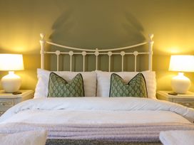 A bed with white bedding and green decorative pillows with two lamps on nightstands at Cartref in Llangernyw