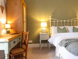 A bedroom with a bed with white linens and green pillows a wooden desk with a lamp and chair and a wooden wardrobe at Cartref in Llangernyw