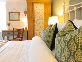A bedroom with a bed with green patterned pillows a wooden wardrobe a desk with a chair and a lamp at Cartref in Llangernyw
