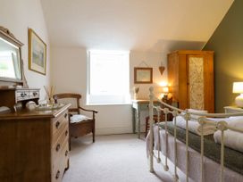 A bedroom with a white metal bed frame wooden dresser wooden chair green desk wooden wardrobe and lamps at Cartref in Llangernyw