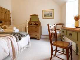 A bedroom with a bed a wooden dresser a mirror two chairs and a table with a vase at Cartref in Llangernyw