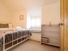 A bedroom with a metal bed frame a window seat a wooden bookshelf and a wooden door at Cartref in Llangernyw