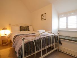 A bedroom with a metal bed frame a bedside table with a lamp a window with shutters and a cushioned window seat at Cartref in Llangernyw