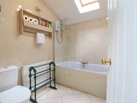 A bathroom with a toilet a bathtub with shower a radiator and a wooden shelf with toiletries at Cartref in Llangernyw