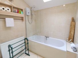 A bathroom with a bathtub shower combination a wooden shelf with toiletries toilet rolls a towel rack and a wooden cutting board decoration at Cartref in Llangernyw