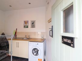 A utility room with a washing machine sink countertop and cleaning tools near the door at Cartref in Llangernyw