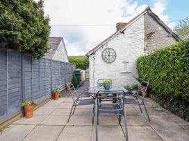 An outdoor patio with a table and four chairs next to a white stone building with a wall clock and surrounded by a wooden fence and hedges at Cartref in Llangernyw