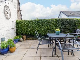 An outdoor patio with a metal table and chairs pots with flowers and a hedge at Cartref in Llangernyw