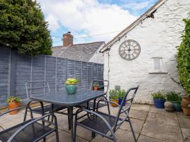 An outdoor patio with a glass table and four metal chairs surrounded by potted plants and a wall clock at Cartref in Llangernyw
