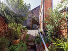 A narrow garden area with potted plants gravel path and a brick house wall at Derwen House in Llangollen