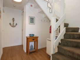 A hallway with carpeted stairs wooden flooring a small wooden table with a bowl on it and wall decorations at Sailing Home in Porthmadog