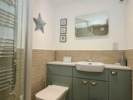 A bathroom with a toilet shower and a sink with cabinets below at Sailing Home in Porthmadog