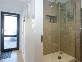 A hallway with a black framed glass door and a shower with glass doors and wooden tiled walls at Sailing Home in Porthmadog