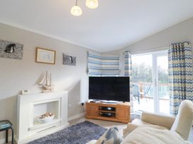 A living room with a television on a wooden stand and sliding glass doors with patterned curtains at Stones Throw in Marston near Barkston