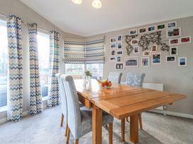 A dining room with a wooden table four upholstered chairs patterned curtains and framed photos on the wall at Stones Throw Marston near Barkston