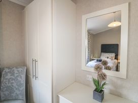 A bedroom reflected in a mirror above a white dresser with a flower pot next to a wardrobe and a patterned chair at Stones Throw in Marston near Barkston