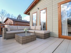 An outdoor deck with a wicker sofa and glass coffee table with flowers at Stones Throw in Marston near Barkston