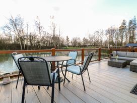 An outdoor deck with a round table and four chairs near a body of water and trees at Stones Throw Marston near Barkston