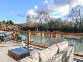 An outdoor seating area with a glass table and chairs by a lake with trees in the background at Stones Throw in Marston near Barkston
