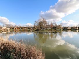 A lake with trees on an island and wooden cabins along the shore at Stones Throw in Marston near Barkston