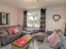 A living room with two grey sofas, a wooden coffee table, a window with plaid curtains and a heart-shaped wall decoration at Lewis Lodge in St Ann's Chapel