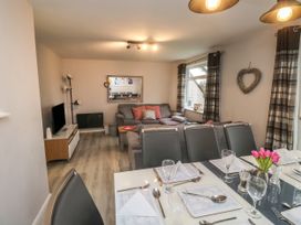 A dining area with table settings and a living room with a sofa and a television at Lewis Lodge in St Anns Chapel