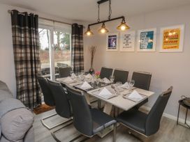 A dining room with a glass table set for eight with black chairs and wall art at Lewis Lodge in St Ann's Chapel