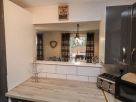 A kitchen countertop with a toaster and microwave and a window opening to a dining area with a table set and plaid curtains at Lewis Lodge in St Ann's Chapel