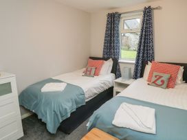 A bedroom with two single beds with folded towels blue blankets and patterned cushions by a window with patterned curtains at Lewis Lodge in St Ann's Chapel