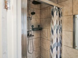 A tiled shower area with a showerhead a shower curtain and a small shelf in a bathroom at Lewis Lodge in St Ann's Chapel