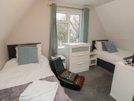 A bedroom with two single beds a window with curtains a white dresser and a gaming chair at Lewis Lodge in St Ann's Chapel
