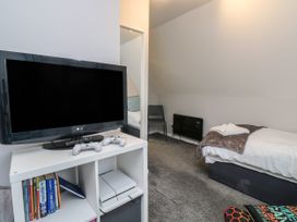 A bedroom with a TV and gaming console on a white shelf a single bed and a chair at Lewis Lodge in St Ann's Chapel
