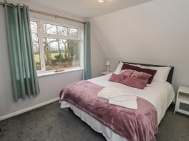 A bedroom with a double bed covered with purple pillows and blanket next to a window with curtains at Lewis Lodge in St Ann's Chapel