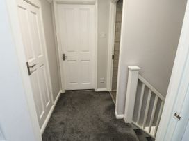A hallway with three white doors grey carpet and a staircase with white railing at Lewis Lodge in St Ann's Chapel