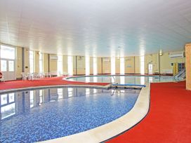 An indoor swimming pool area with two pools surrounded by red carpet and white plastic chairs at Lewis Lodge in St Ann's Chapel