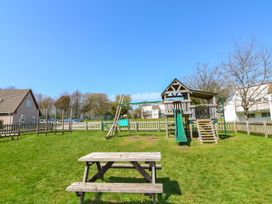 A playground with a wooden climbing frame and slide and a wooden picnic table on grass at Lewis Lodge in St Ann's Chapel