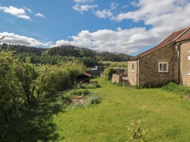 A grassy garden with shrubs and a stone building beside it with hills and trees in the background at White Lodge Cottage in Scalby