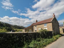 A stone house with a tiled roof next to a stone wall and grassy area under a blue sky at White Lodge Cottage in Scalby