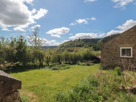 A garden with grass and bushes beside a stone house in a rural area at White Lodge Cottage in Scalby