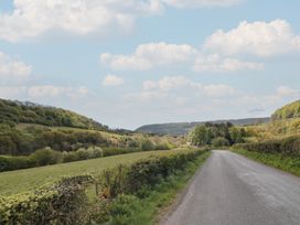A country road with hedges on both sides surrounded by fields and hills with trees under a cloudy sky at White Lodge Cottage in Scalby